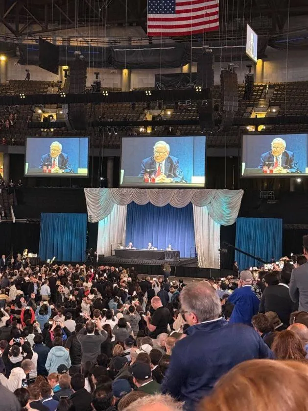 Warren Buffett on stage on the big screens at a packed shareholder meeting
