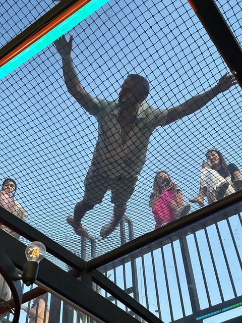Me spread out on a rooftop net, seen from below, with friends watching