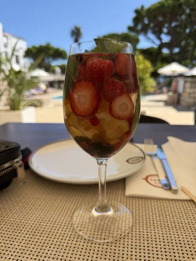 A glass of sangria with strawberries beside a pool